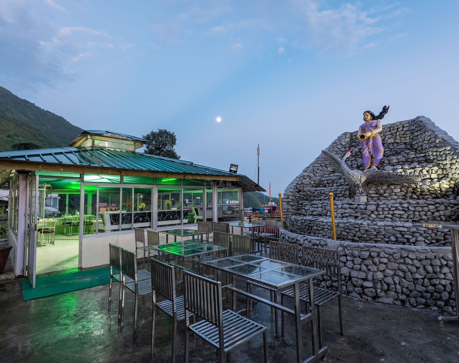 A view of an outdoor dining area at a resort with a stone fountain and a statue in the foreground -  DLS Meghavan Resort